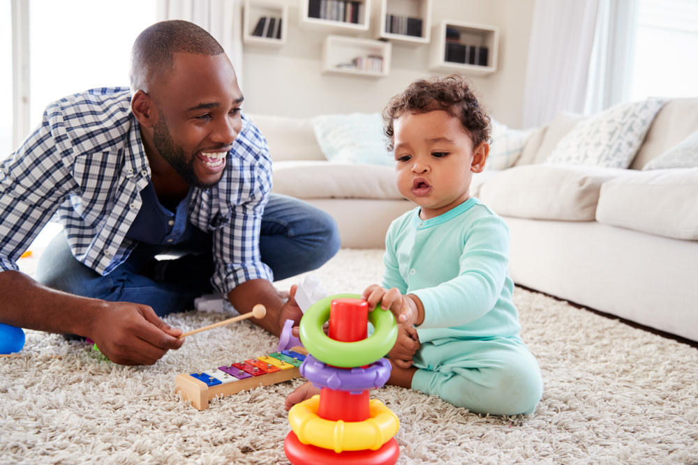 An African American Father interacting with his infant child with toys.