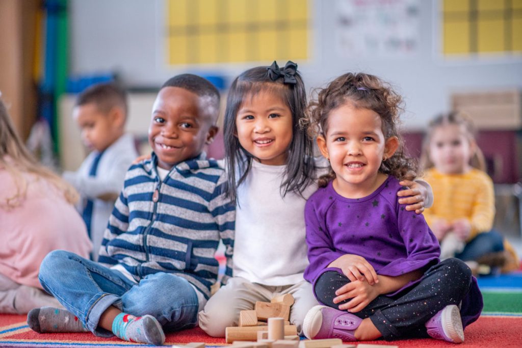 three interracial kids smiling with their arms around each other